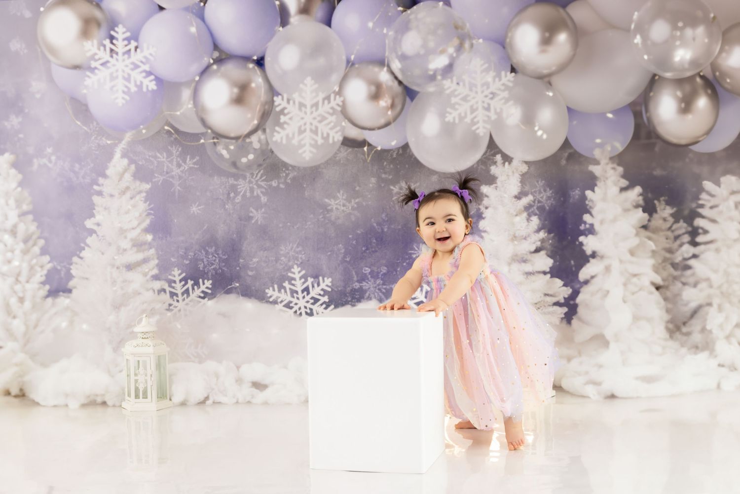 Enchanting winter wonderland scene with white trees, sparkling balloons and snowflakes in a dreamy purple and white setting.