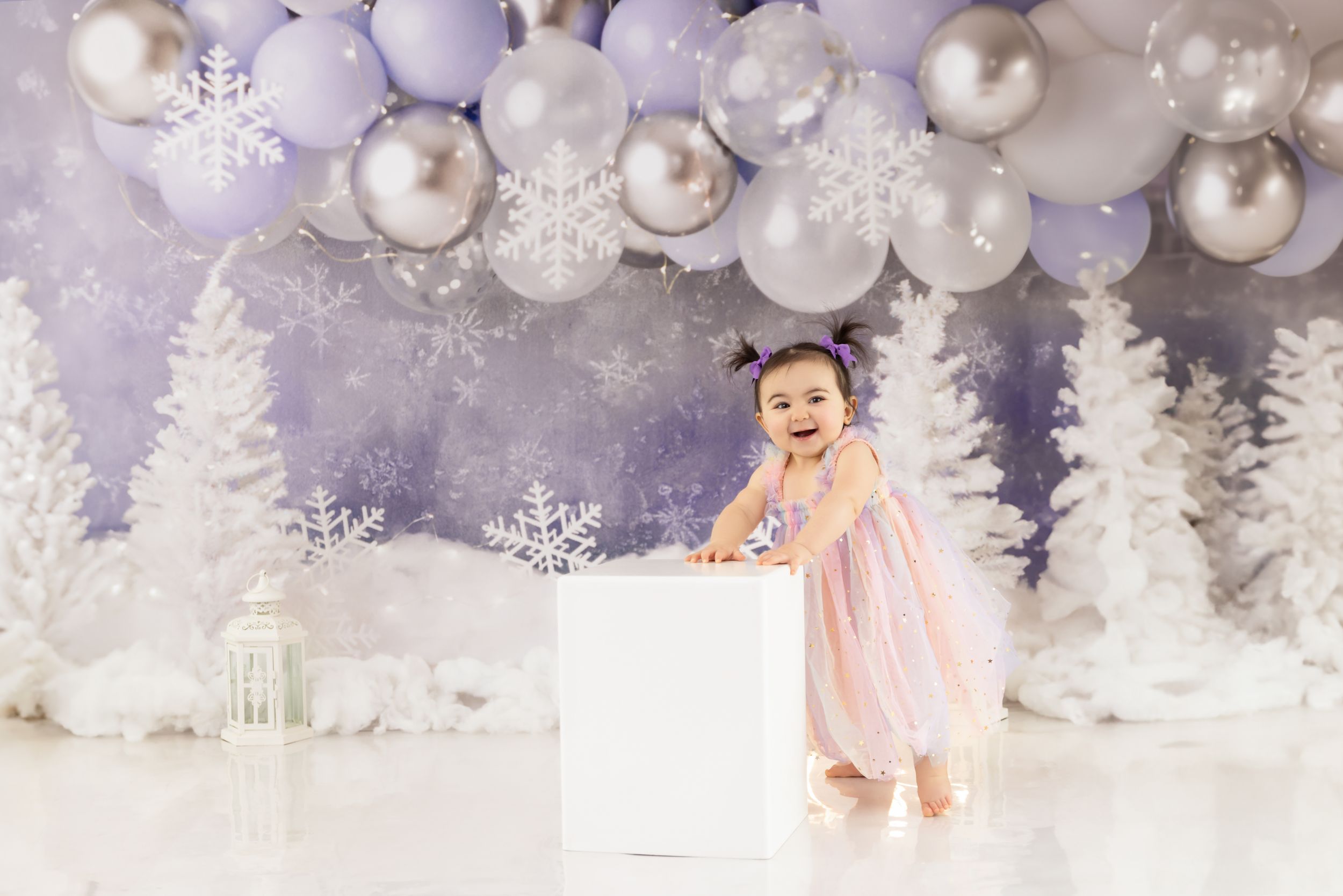 Enchanting winter wonderland scene with white trees, sparkling balloons and snowflakes in a dreamy purple and white setting.