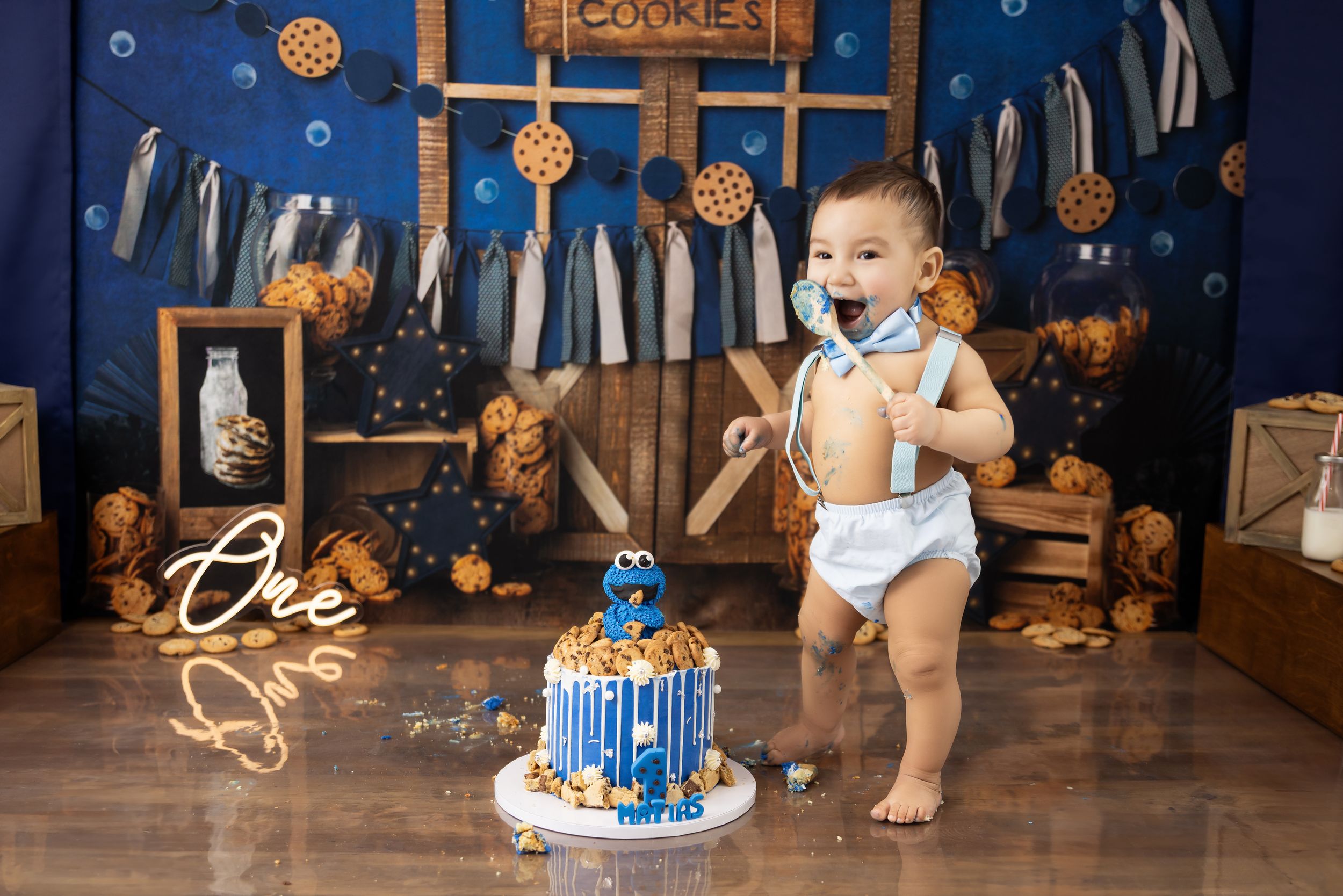 A festive first birthday cake smash setup with a blue and gold theme featuring a decorated cake and rustic wooden backdrop.