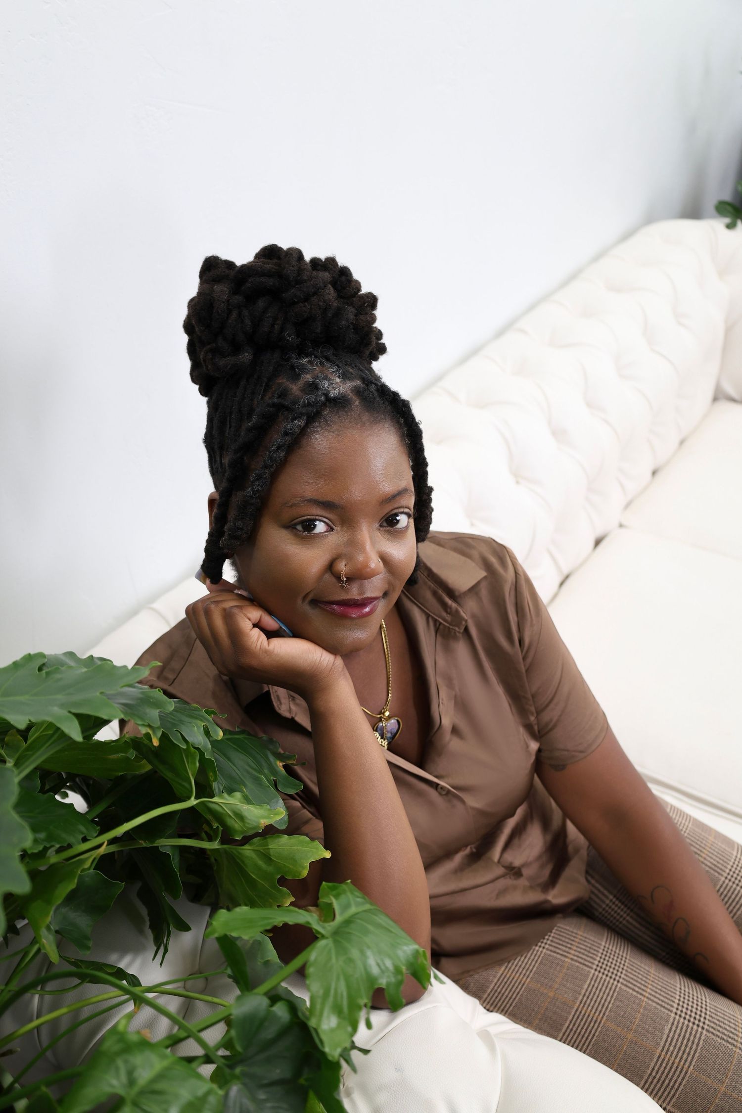 Stylish individual relaxes on white couch next to potted plants in elegant home setting.