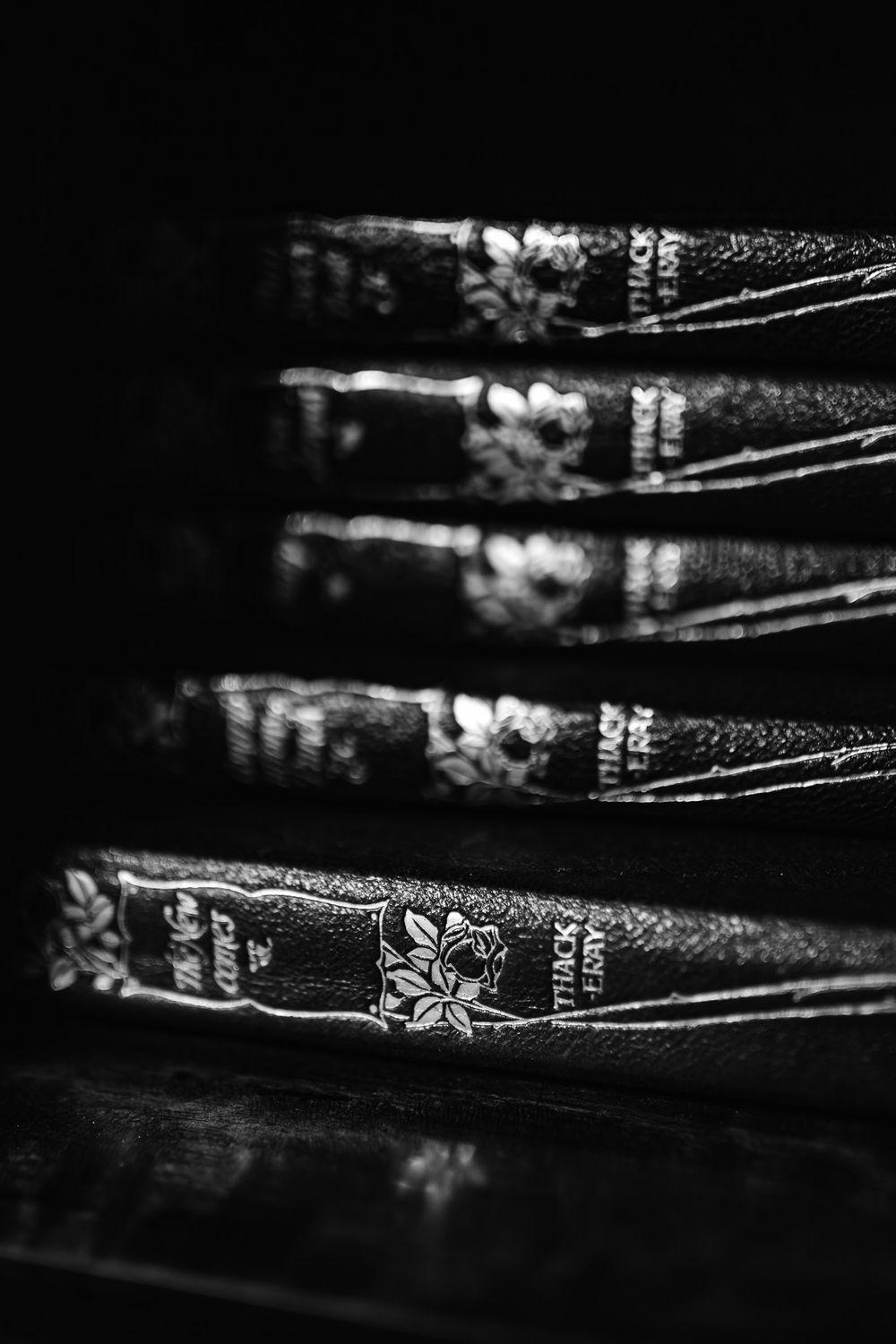 Stack of antique leather-bound books with embossed floral designs photographed in dramatic black and white lighting.