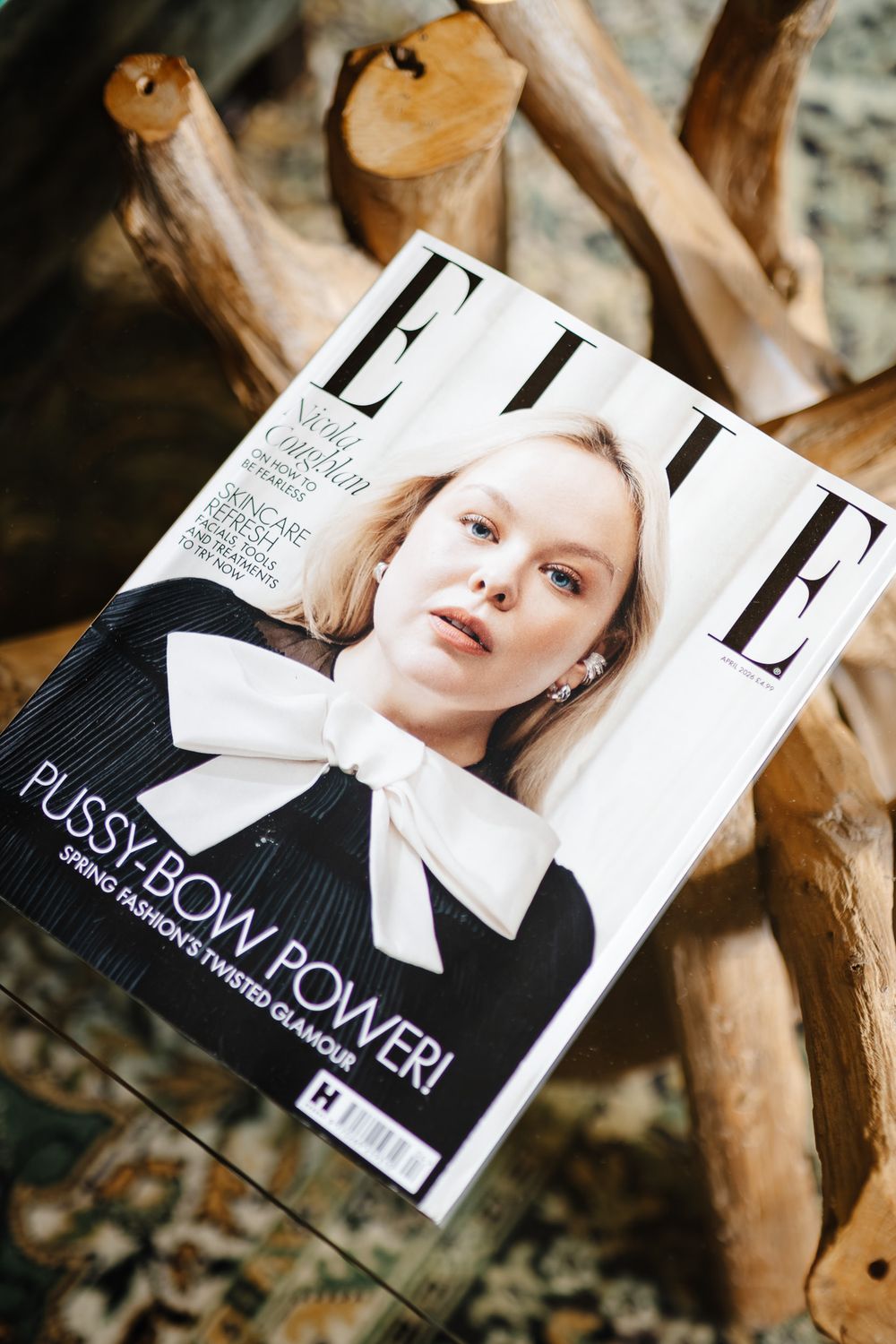 ELLE magazine cover featuring Nicola Coughlan in a black top with white pussy-bow, resting on rustic wooden logs.