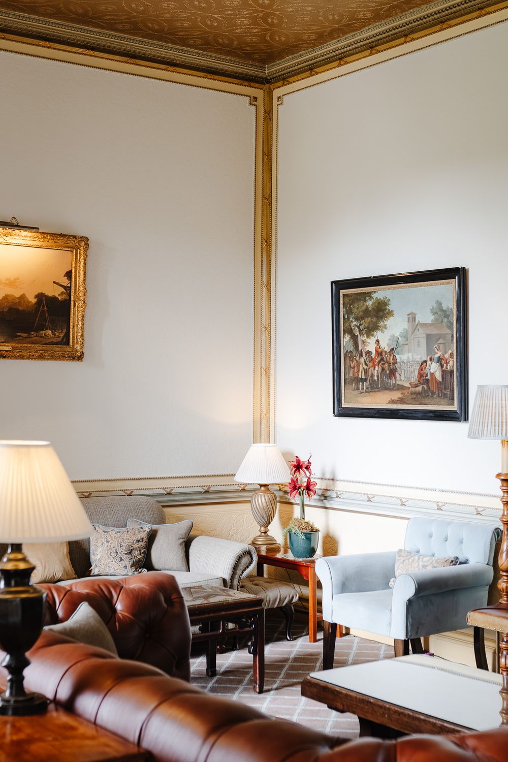 Elegant traditional living room with leather sofas, classic paintings, ornate gold moldings, and table lamps in a grand interior.