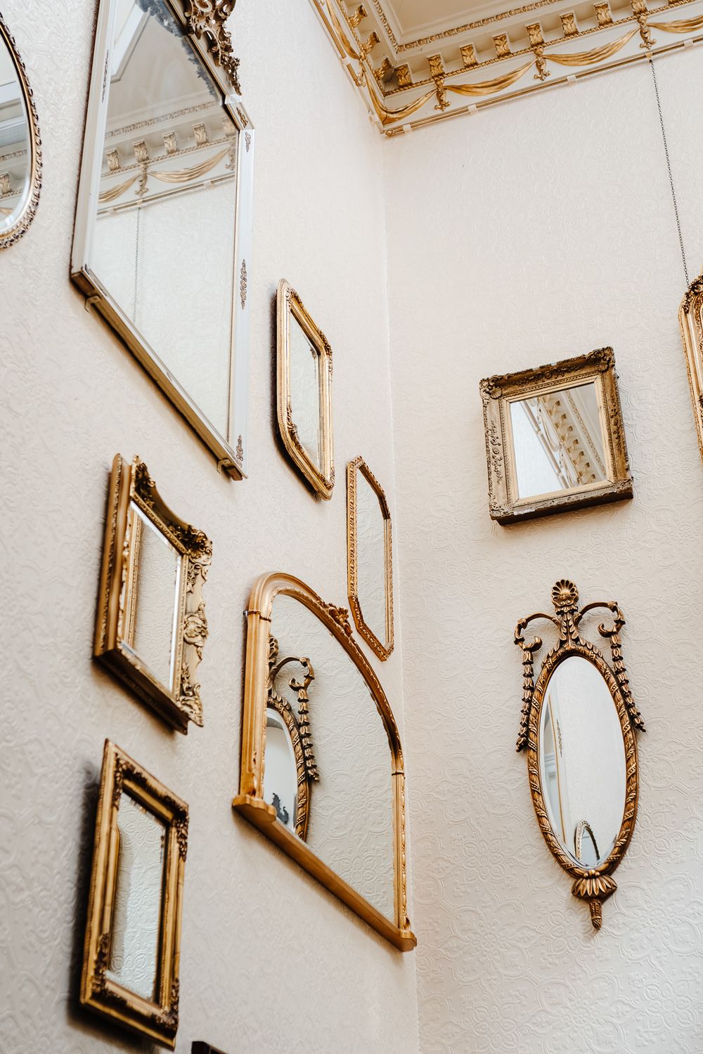 Collection of ornate gold-framed mirrors arranged on white walls in an elegant corner display.