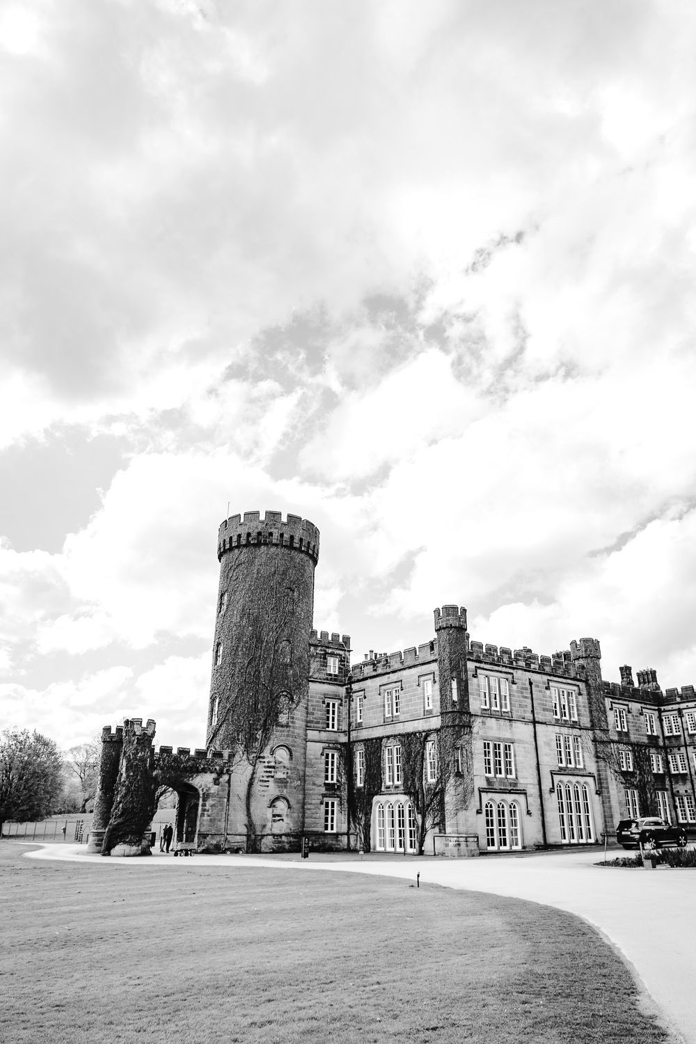 Black and white photo of a historic stone castle with round tower under dramatic cloudy sky.