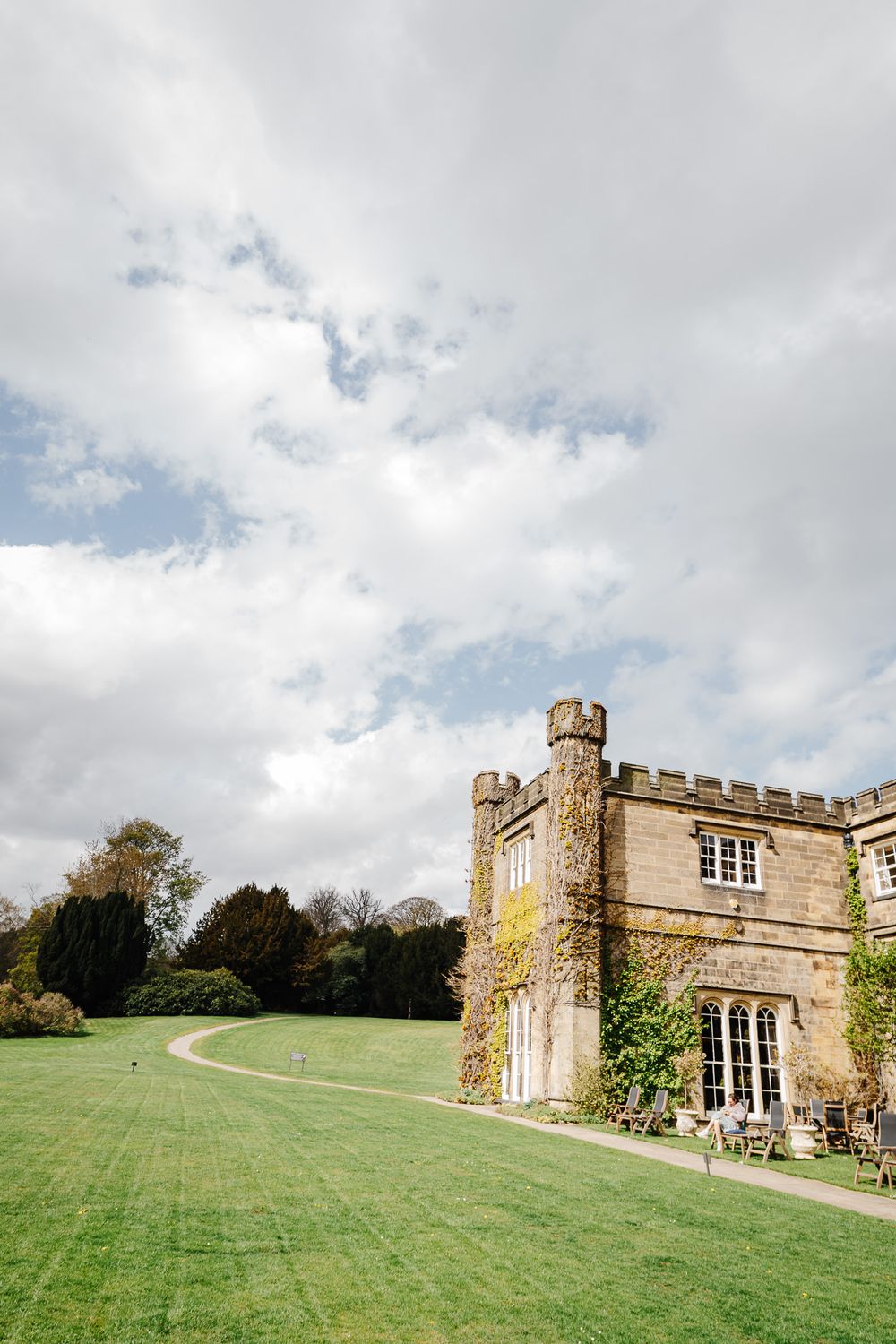 Historic English castle with ivy-covered stone walls and battlements set against a vast green lawn under cloudy skies.