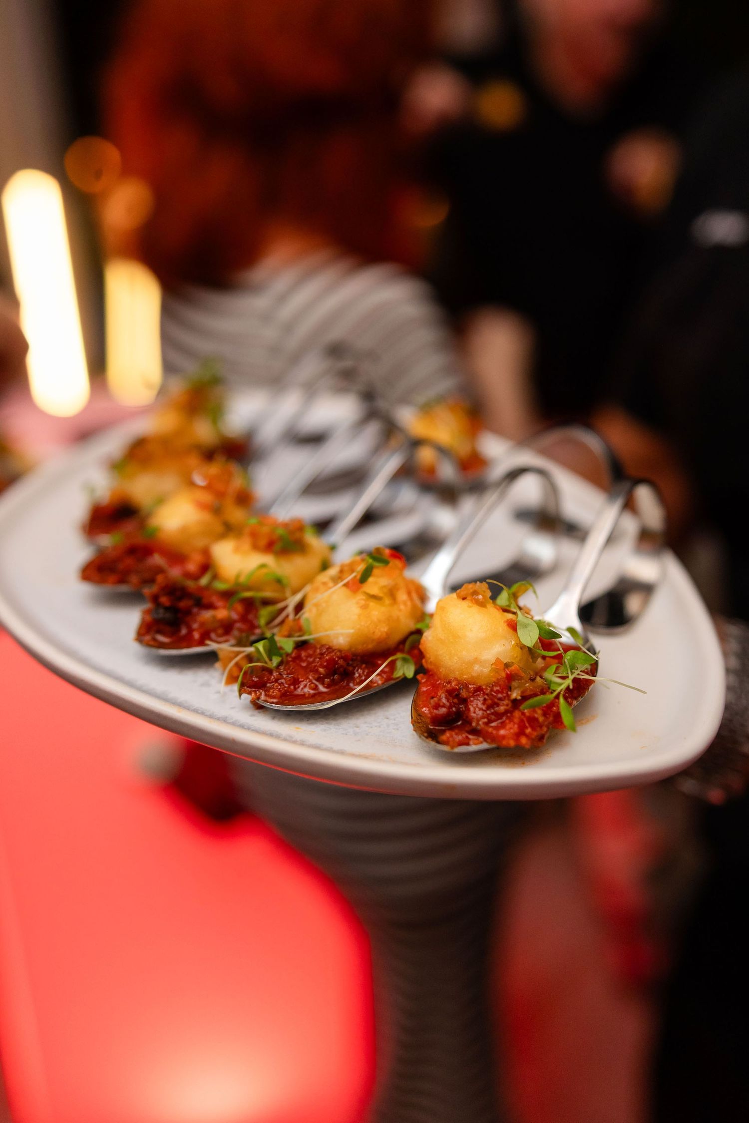 Elegant appetizer spoons with crispy scallops on savory sauce, garnished with microgreens, served on a platter at upscale event.