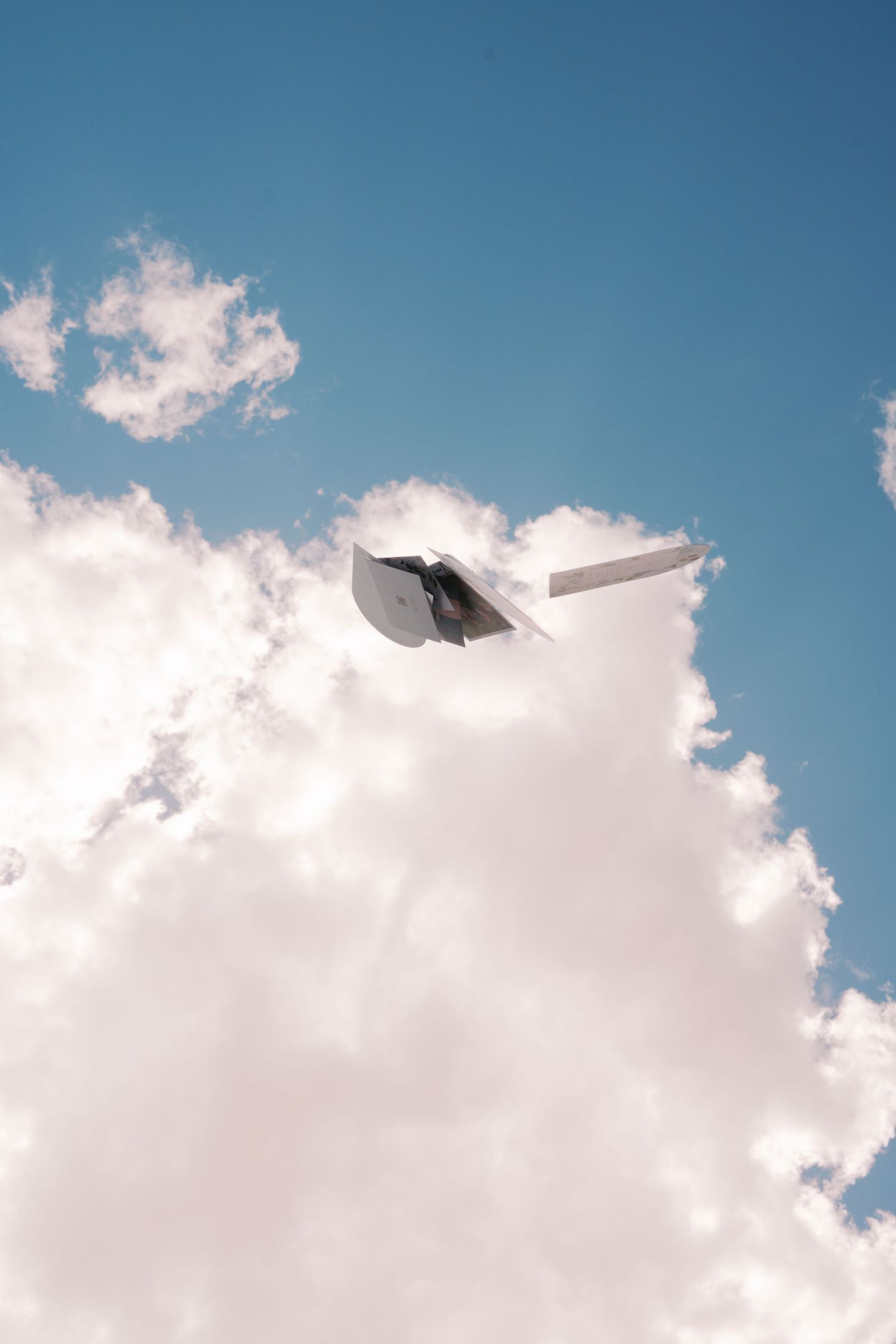 A white paper airplane soaring through a bright blue sky with fluffy white clouds below it.
