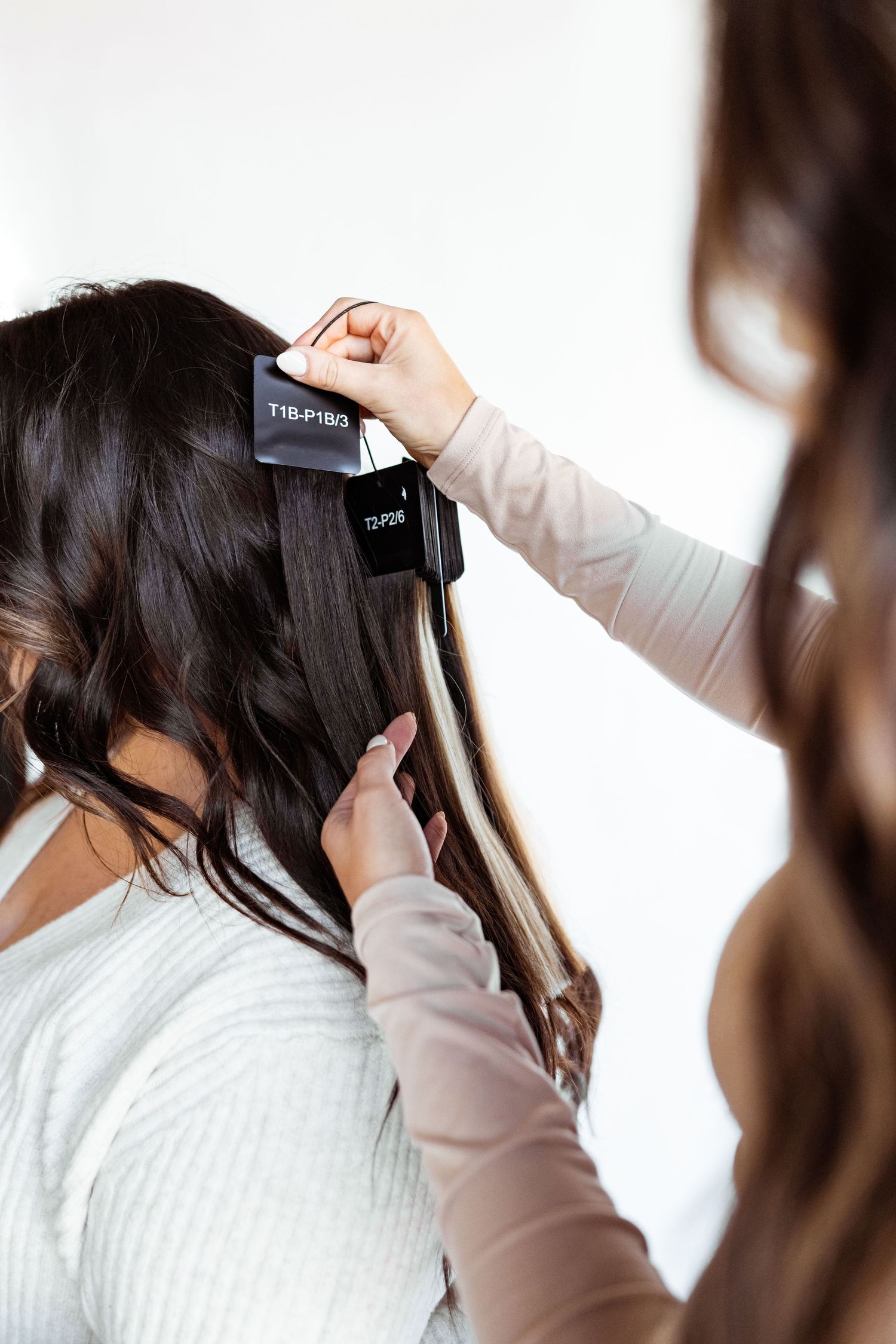 Hairstylist using a flat iron to straighten dark brunette hair with blonde highlights in a salon setting.