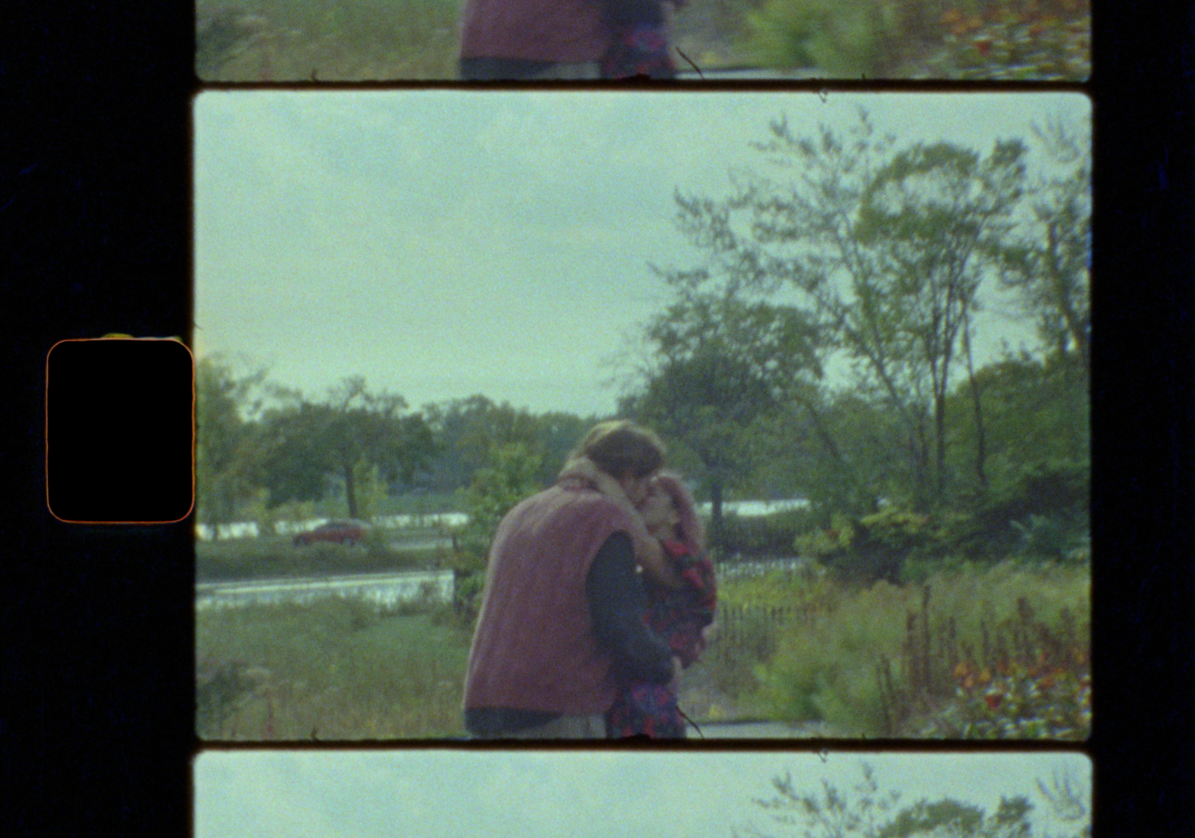 Vintage film strip showing two people embracing near a serene lake surrounded by lush green trees.