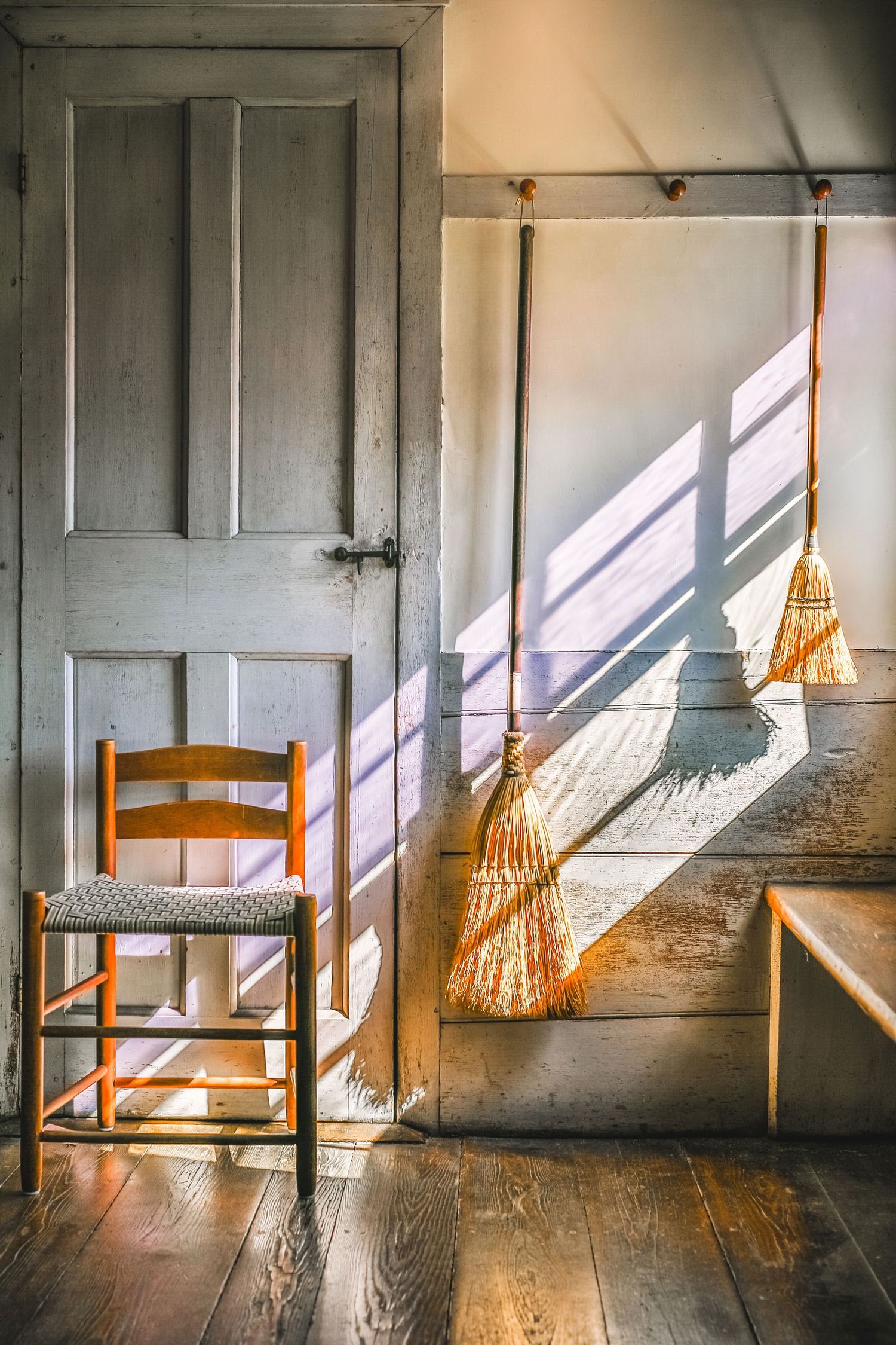 Shaker brooms hang from a wall with a light blue door with broom shadows at Canterbury Shaker Village. New England photographer