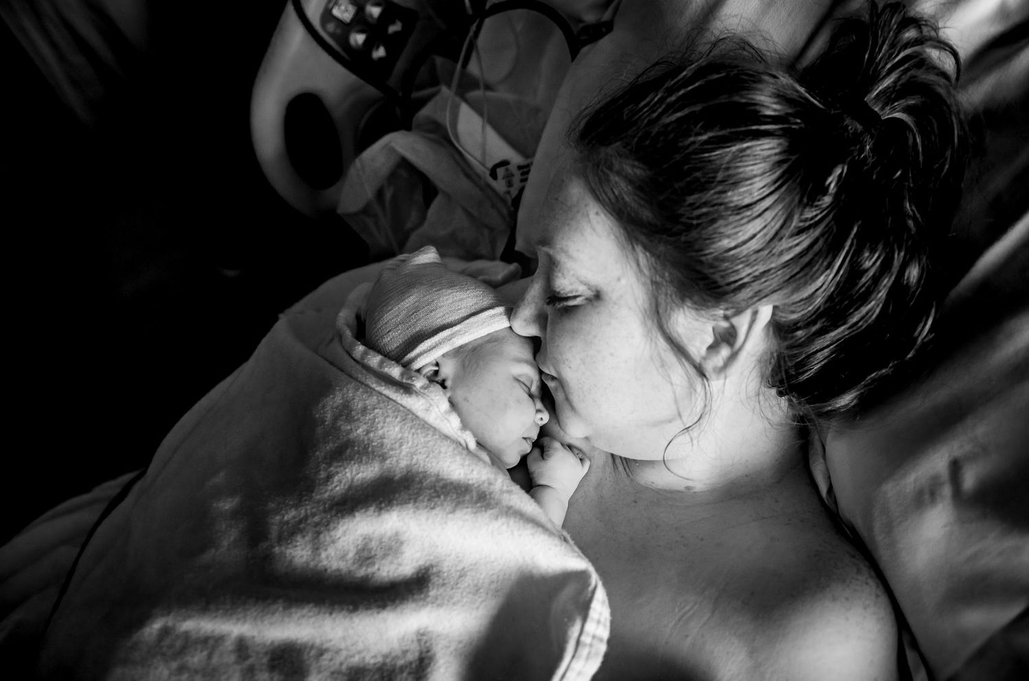 An intimate black and white photograph captures a tender moment of connection in a hospital room.