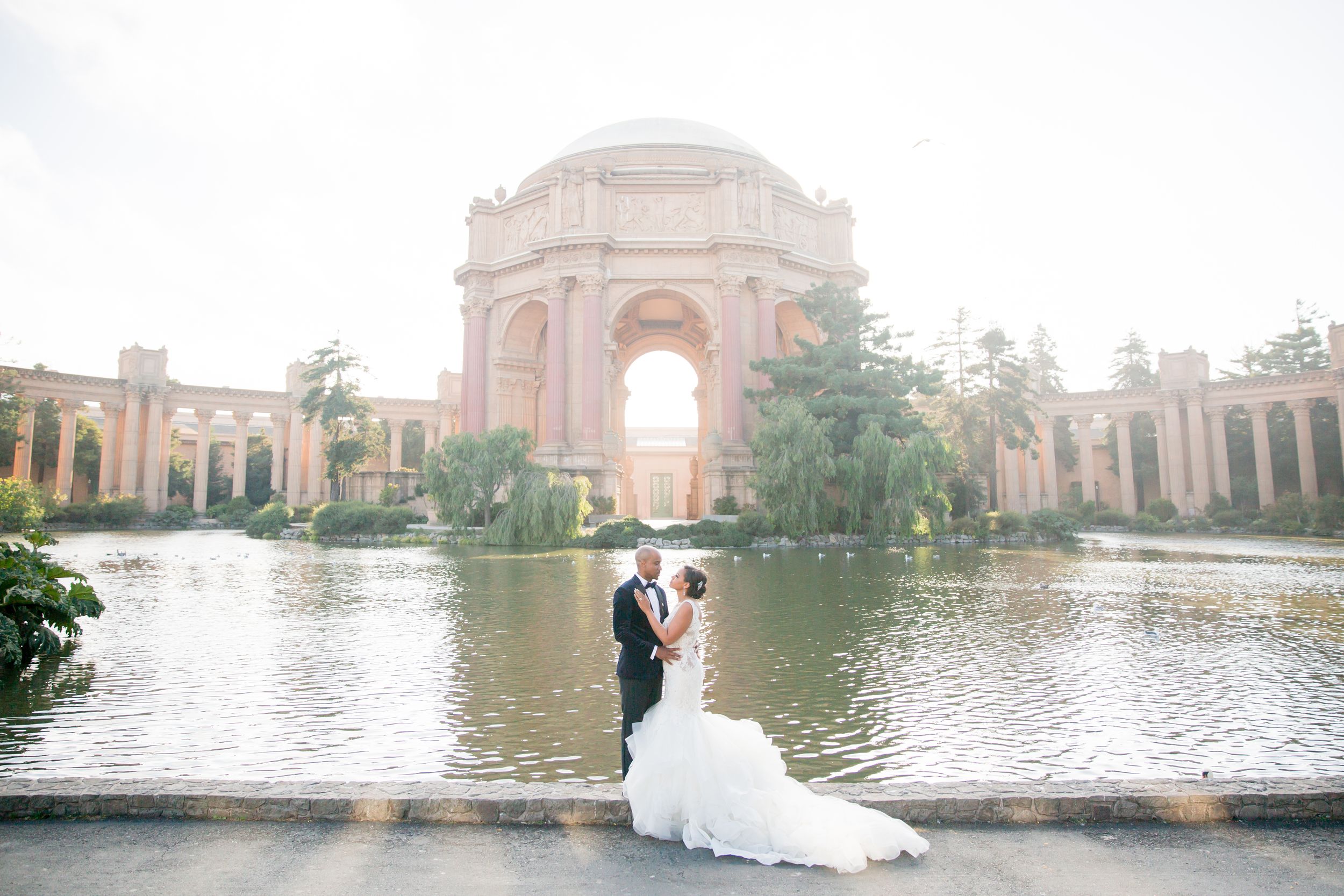 Bride and groom embracing in front of the Palace of Fine Arts lagoon in San Francisco on their wedding day.