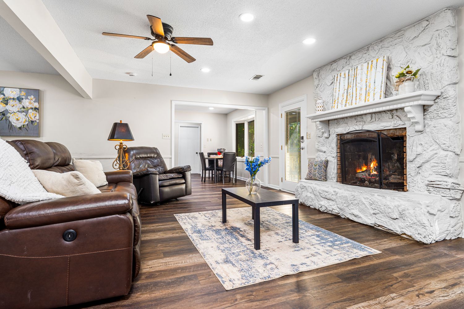 Cozy living room with brown leather recliners, stone fireplace, hardwood floors, and ceiling fan.