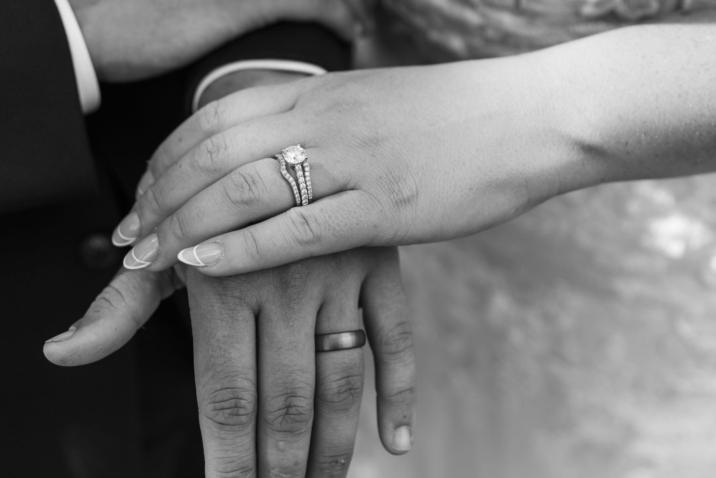 Black and white photo of newlyweds hands showing diamond engagement ring and wedding bands.
