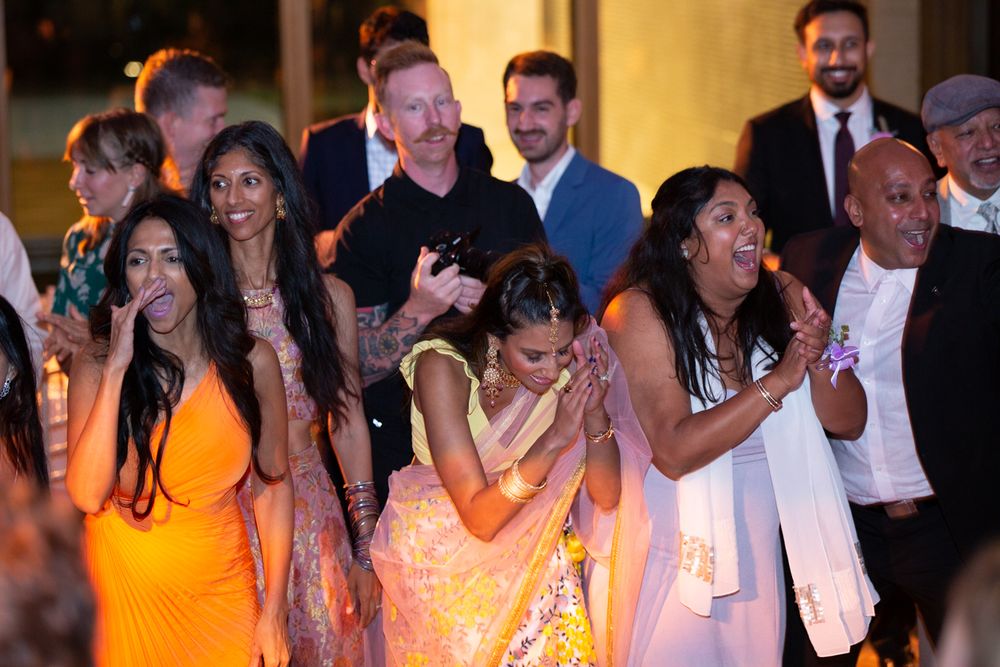 Joyful guests in colorful attire react with excitement at an Indian wedding celebration outdoors.