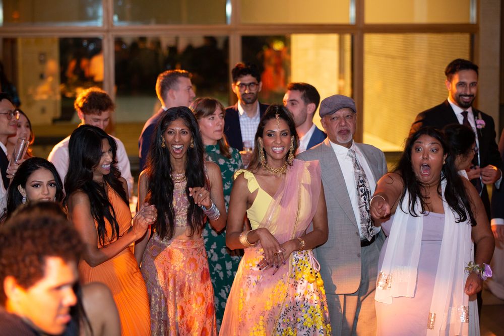 Diverse group of guests in colorful traditional attire dancing and celebrating at an elegant indoor wedding reception.
