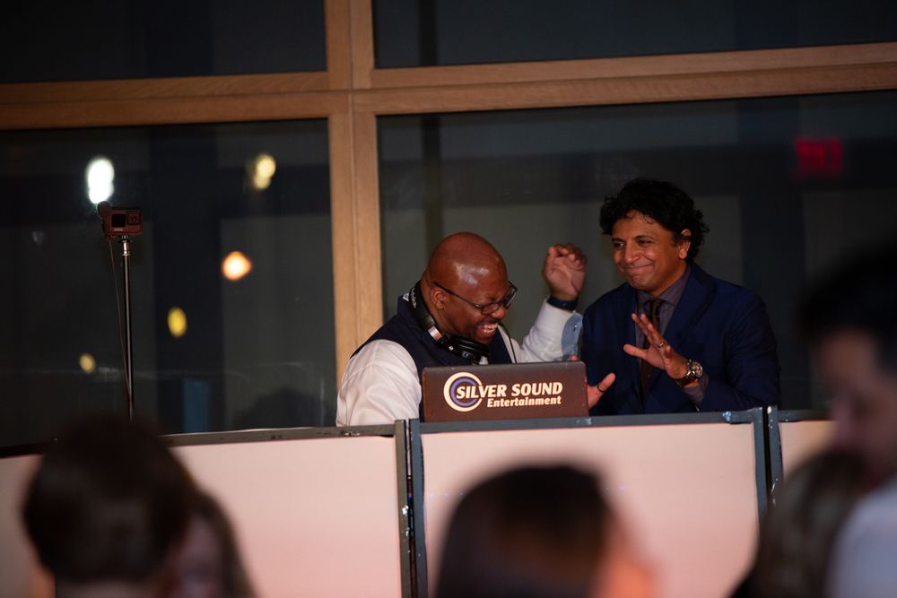 Two men conversing animatedly at a Silver Sound Entertainment DJ booth during an evening event.