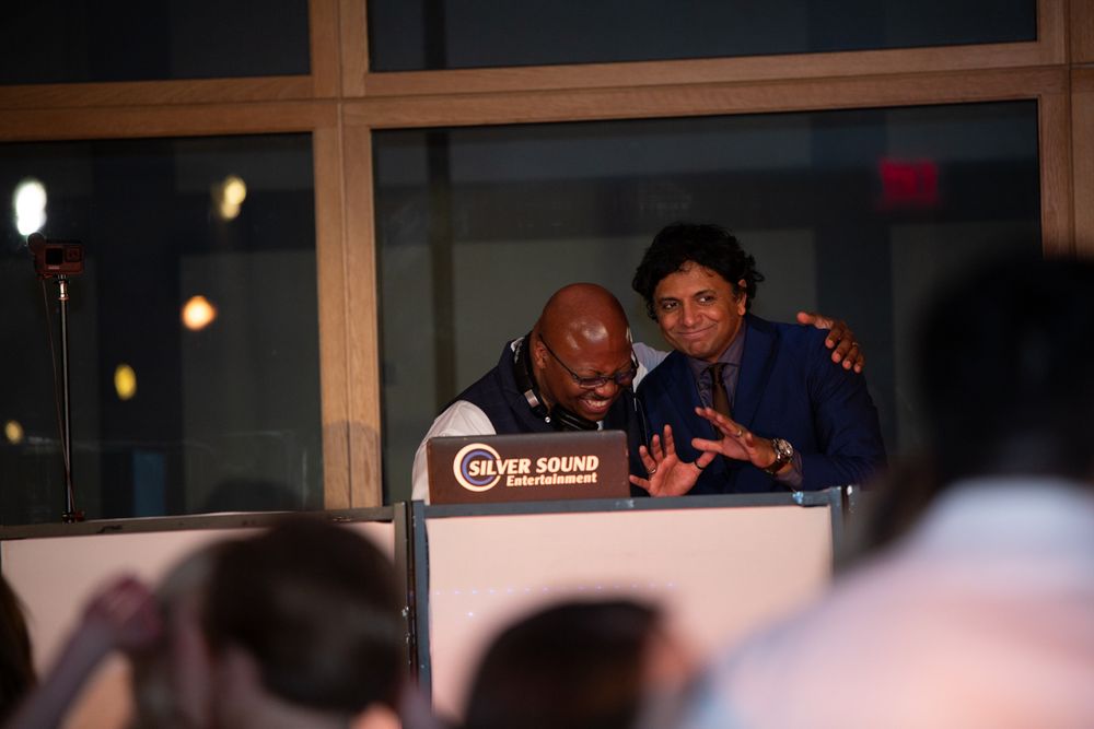 Two DJs smiling and performing behind a Silver Sound Entertainment booth at an indoor event.