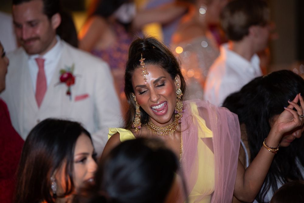 Bride in yellow and pink saree with gold jewelry laughs joyfully at her wedding reception.