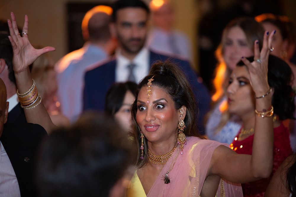 Woman in pink saree with gold jewelry dances joyfully at an Indian wedding reception.