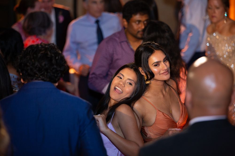 Two women smiling and posing together at a lively indoor party or wedding reception.