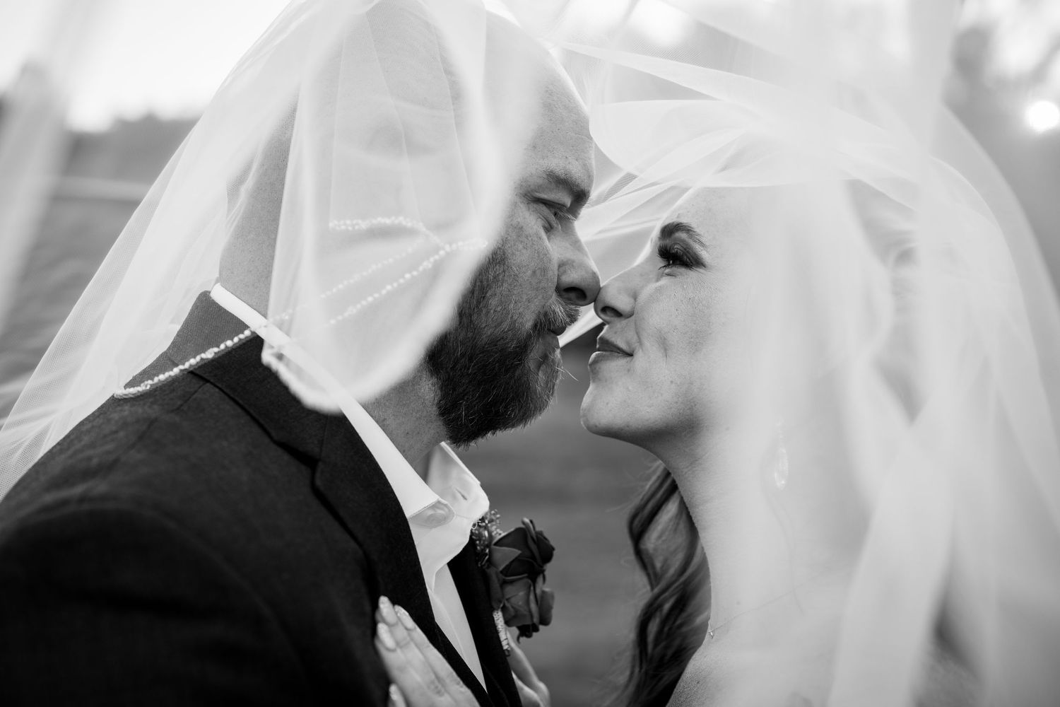 Black and white photo of bride and groom kissing under wedding veil.