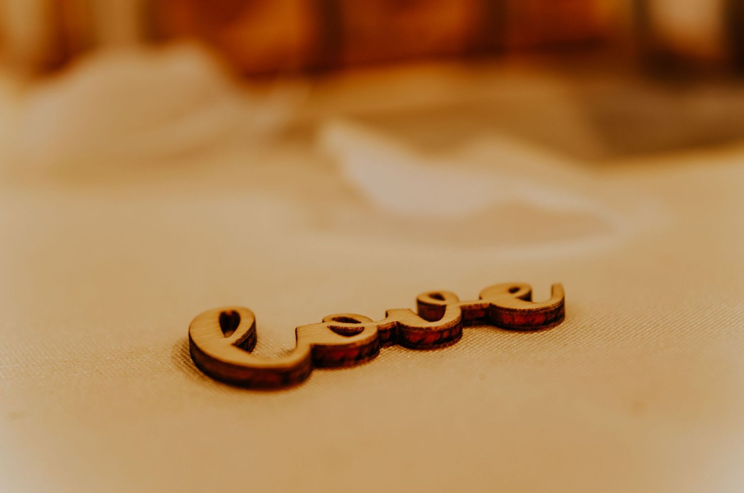 Wooden laser-cut 'Love' sign resting on a soft beige surface with warm bokeh background lighting.