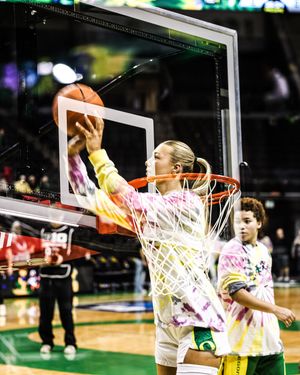Oregon Ducks female basketball player in tie-dye shirt cuts the net after a victory celebration at Matthew Knight Arena.