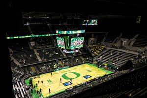 Aerial view of University of Oregon basketball arena with green court, large scoreboard, and seating under dramatic lighting.