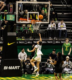 Oregon Ducks player #2 attempts a layup during a college basketball game at a packed arena with Taco Bell and Bi-Mart ads.