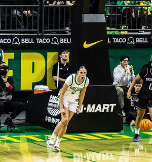 Oregon Ducks women's basketball player dribbles up court in green uniform at Nike-sponsored arena game.