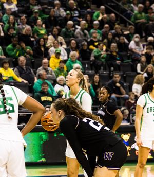 Oregon Ducks women's basketball player battles Washington Huskies defender for possession during an indoor college game.