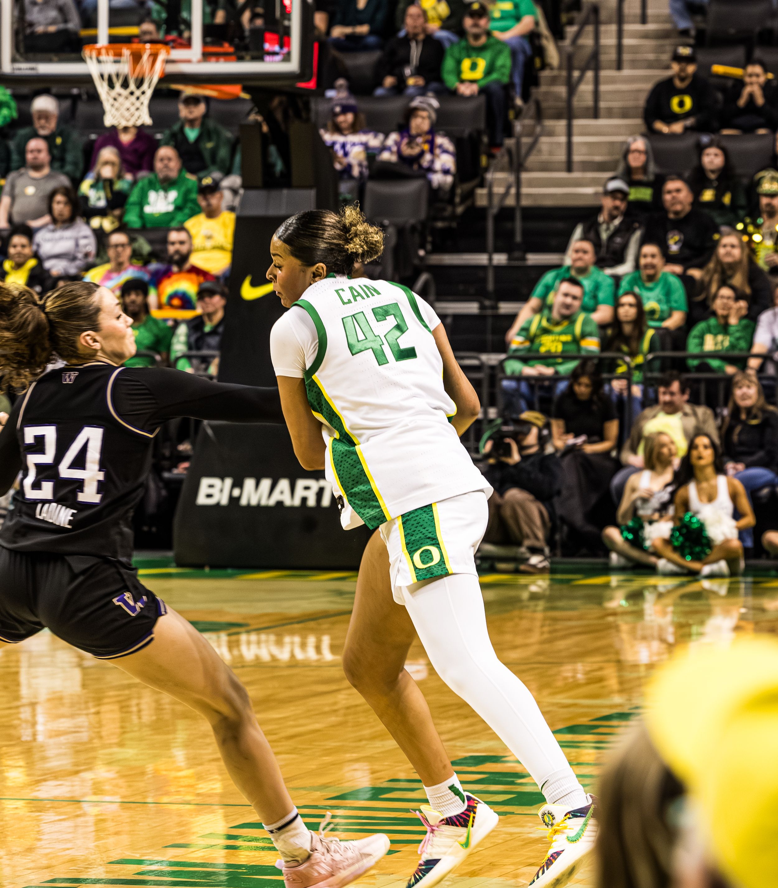 Oregon Ducks player #42 defends against opponent #24 during a women's college basketball game at a packed arena.