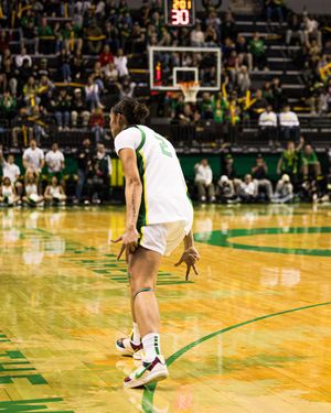 Basketball player in white uniform dribbles on indoor court with green and yellow arena decor.