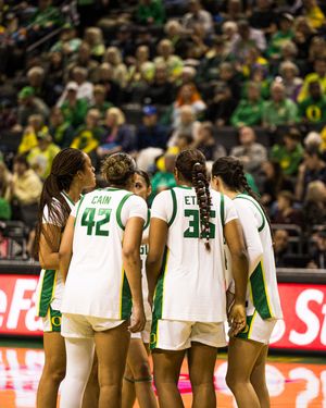 Oregon Ducks women's basketball players huddle on court wearing green and white uniforms during a home game.