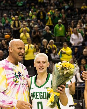 Oregon Ducks player #0 holds flowers with a fan during a senior day ceremony at a home basketball game.