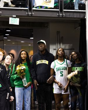 Oregon Ducks basketball players and staff gather in green and white uniforms during a senior day ceremony inside an arena.