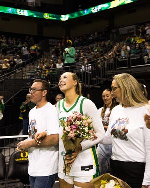 Oregon Ducks basketball player holding flowers with family during senior night ceremony at Matthew Knight Arena.