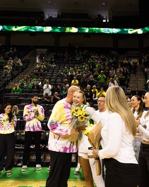 Oregon Ducks basketball player receives flowers from family during senior night ceremony at packed arena.