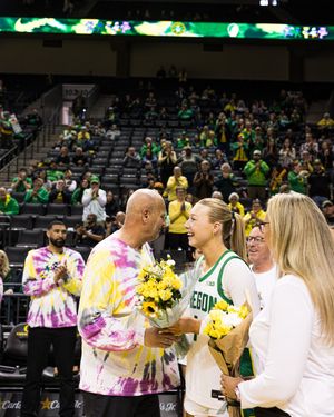 Oregon Ducks basketball player receives flowers from family during senior night ceremony at packed arena.