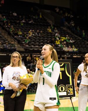 Oregon Ducks basketball player #1 speaks at microphone during senior night ceremony with flowers and framed jersey.