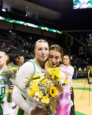 Oregon Ducks women's basketball player hugs teammate while holding sunflower bouquet at senior night.