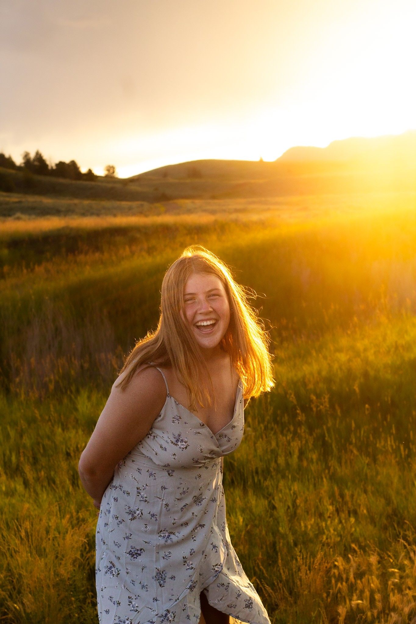Young woman in denim vest and black skirt smiling by a serene pond surrounded by lush green autumn trees.