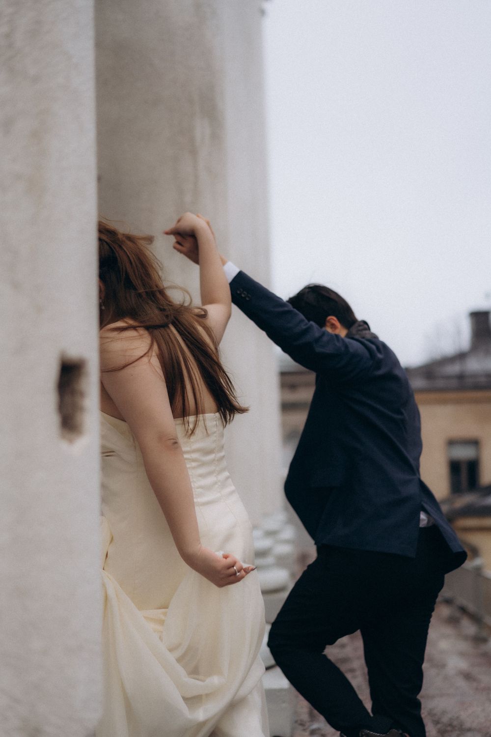 Playful engaged couple leaning against a white column at Helsinki Cathedral during a Helsinki engagement photoshoot