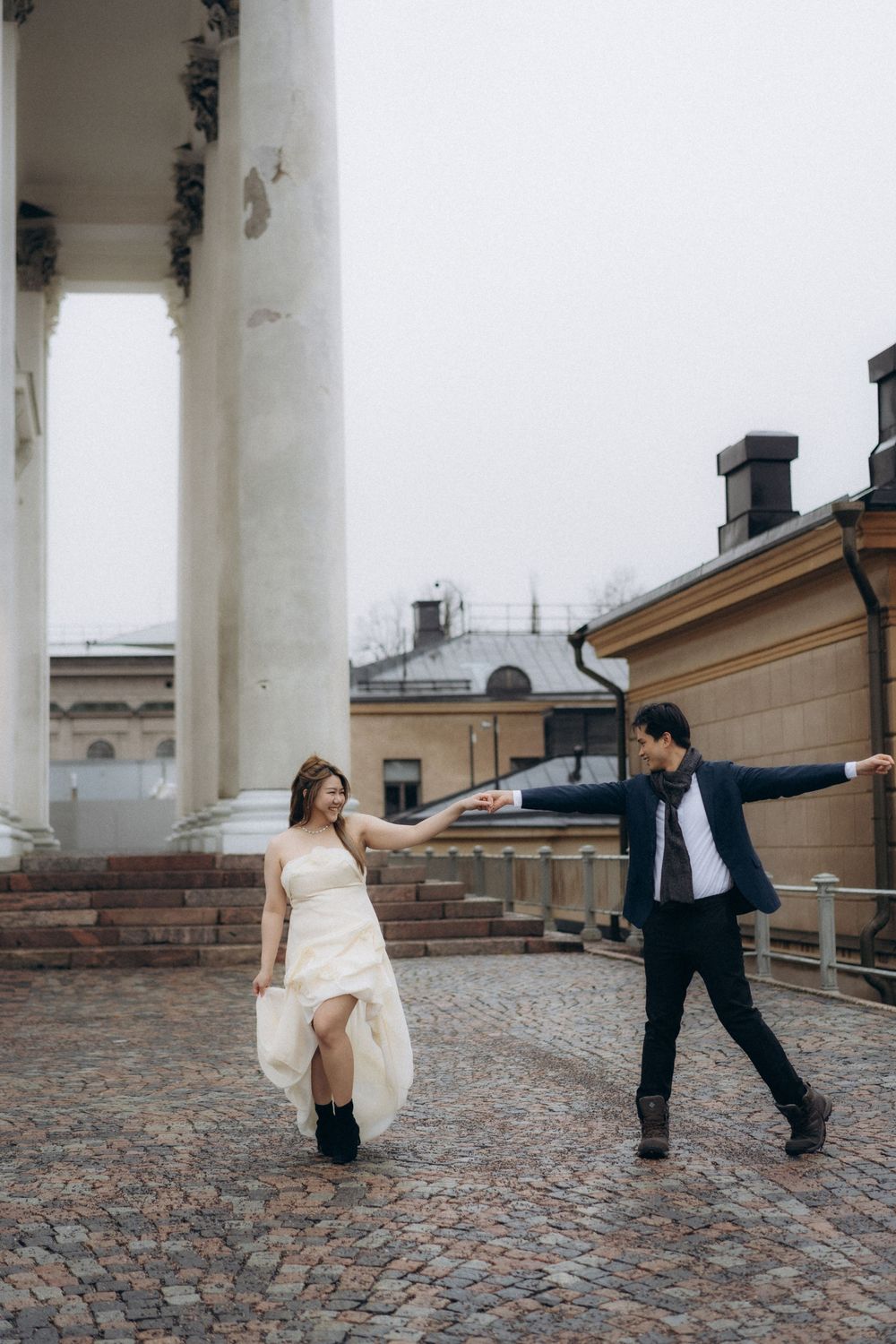 Engaged couple running across Senate Square by Helsinki Cathedral during a natural engagement session
