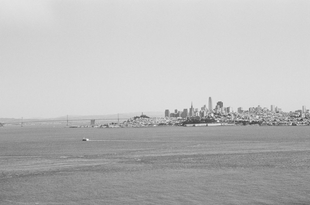 Black and white aerial view of San Francisco skyline and Golden Gate Bridge from the bay.