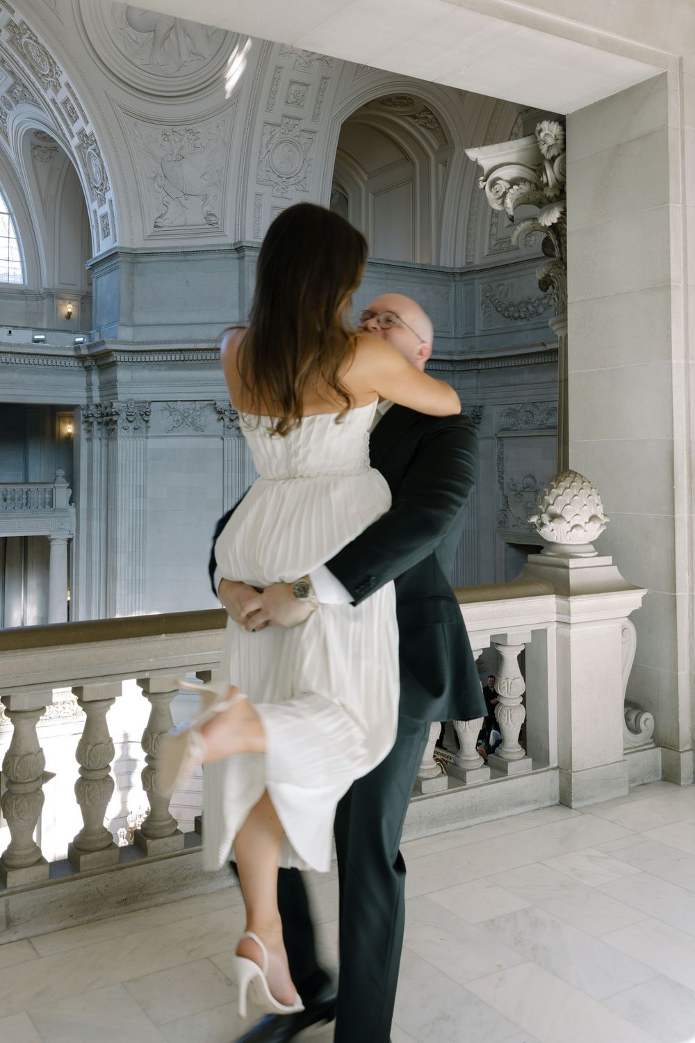 A couple embraces and dances in an elegant marble building interior during their wedding ceremony.
