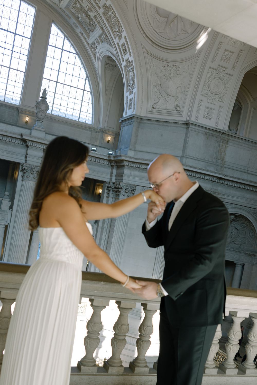 Groom kissing bride's hand during intimate wedding ceremony at San Francisco City Hall with ornate architecture.