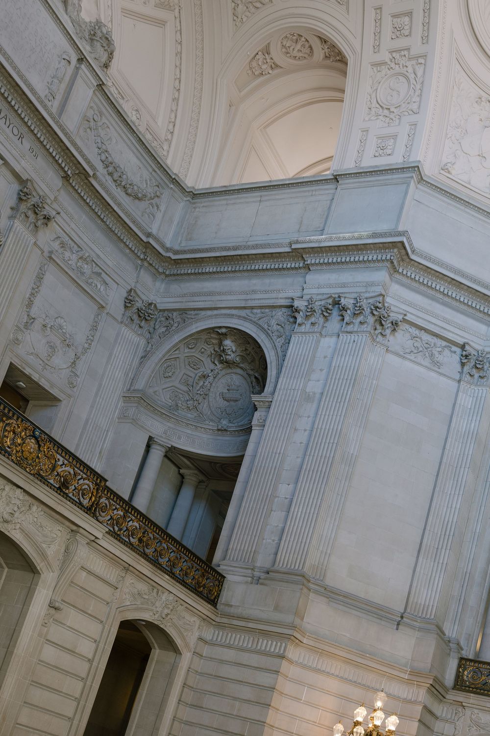 Grand marble interior of a classical government building featuring ornate columns, decorative friezes, and an elegant chandelier.